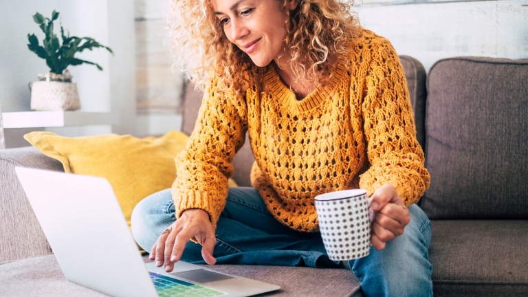 Engaged employee in yellow sweater works on laptop while sitting on her couch | Reduce Labor Costs