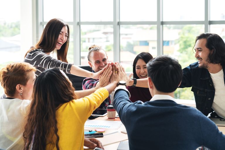 Engaged employees place hands in a circle during team meeting | Improve employee retention